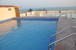 A swimming pool with a metal ladder, a sign indicating a 1:50 depth ratio, and a view of the ocean.