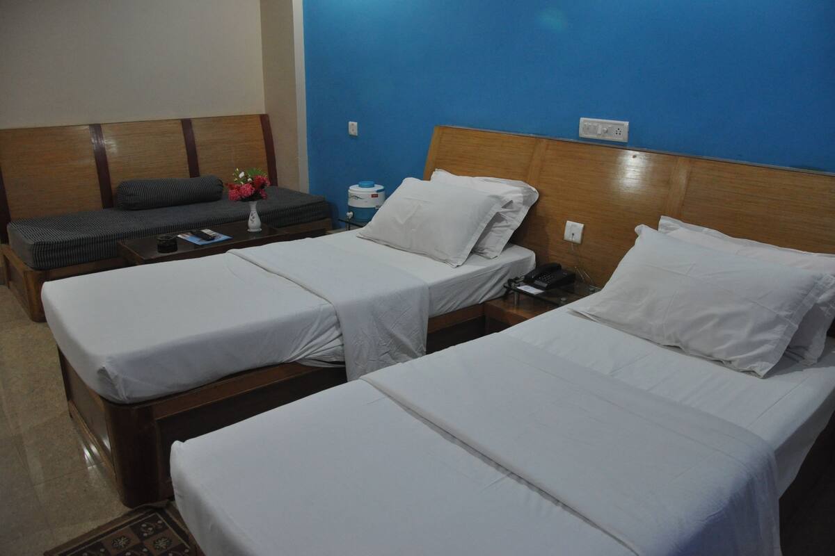 Una habitación de hotel con dos camas individuales, una mesita con un florero y un banco.