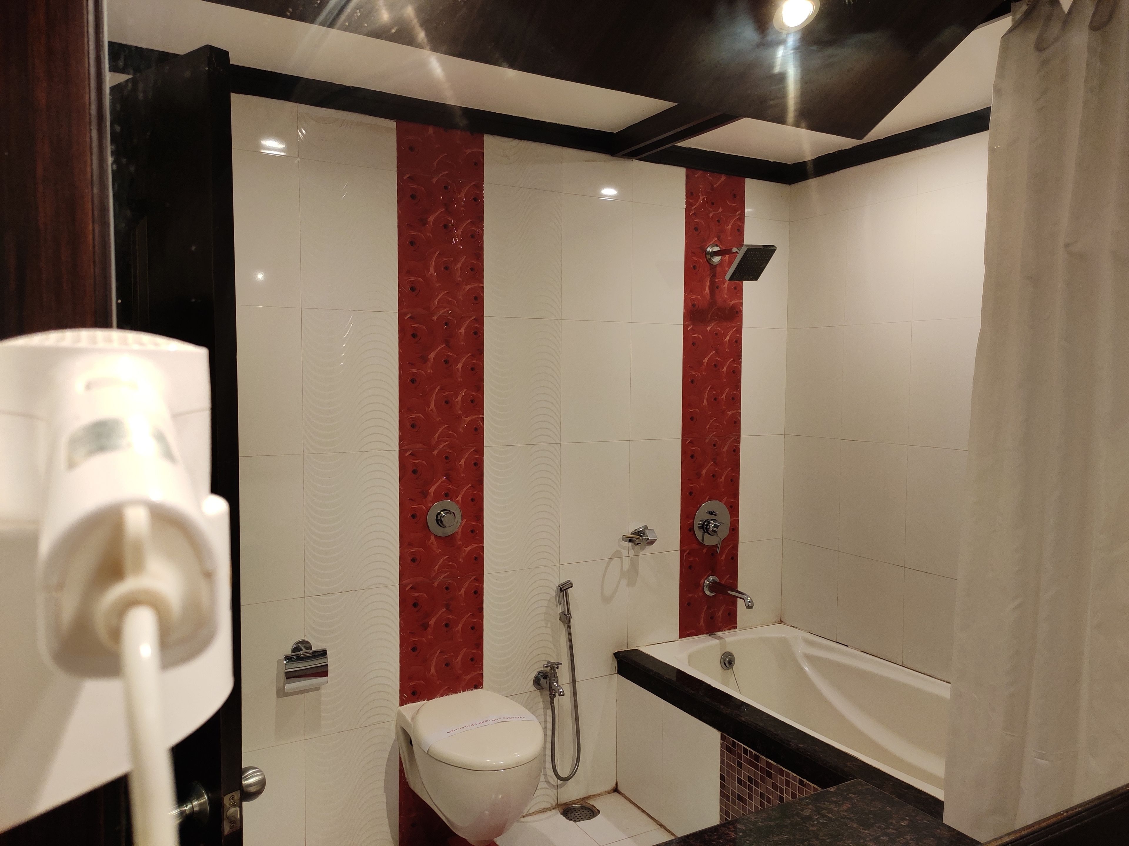 Un baño moderno con un revestimiento de azulejos blancos y rojos, un inodoro blanco, una bañera y una zona de ducha.