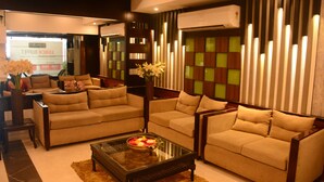 A modern living room with two beige sofas, a glass coffee table, and a decorative vase. - Hotel Pushpak (Bhubaneshwar)