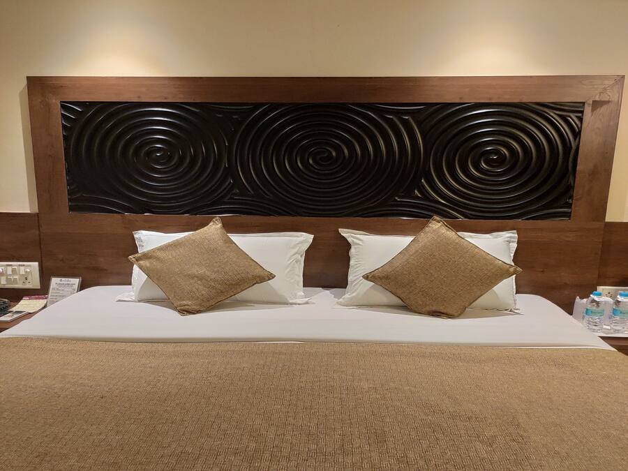 Una habitación de hotel con una cama grande, dos almohadas, un cabecero con diseño circular negro y una alfombra marrón con textura.