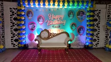 Un escenario con alfombra roja estampada, un sofá blanco y un fondo decorado con el texto 'Happy Birthday' y globos.