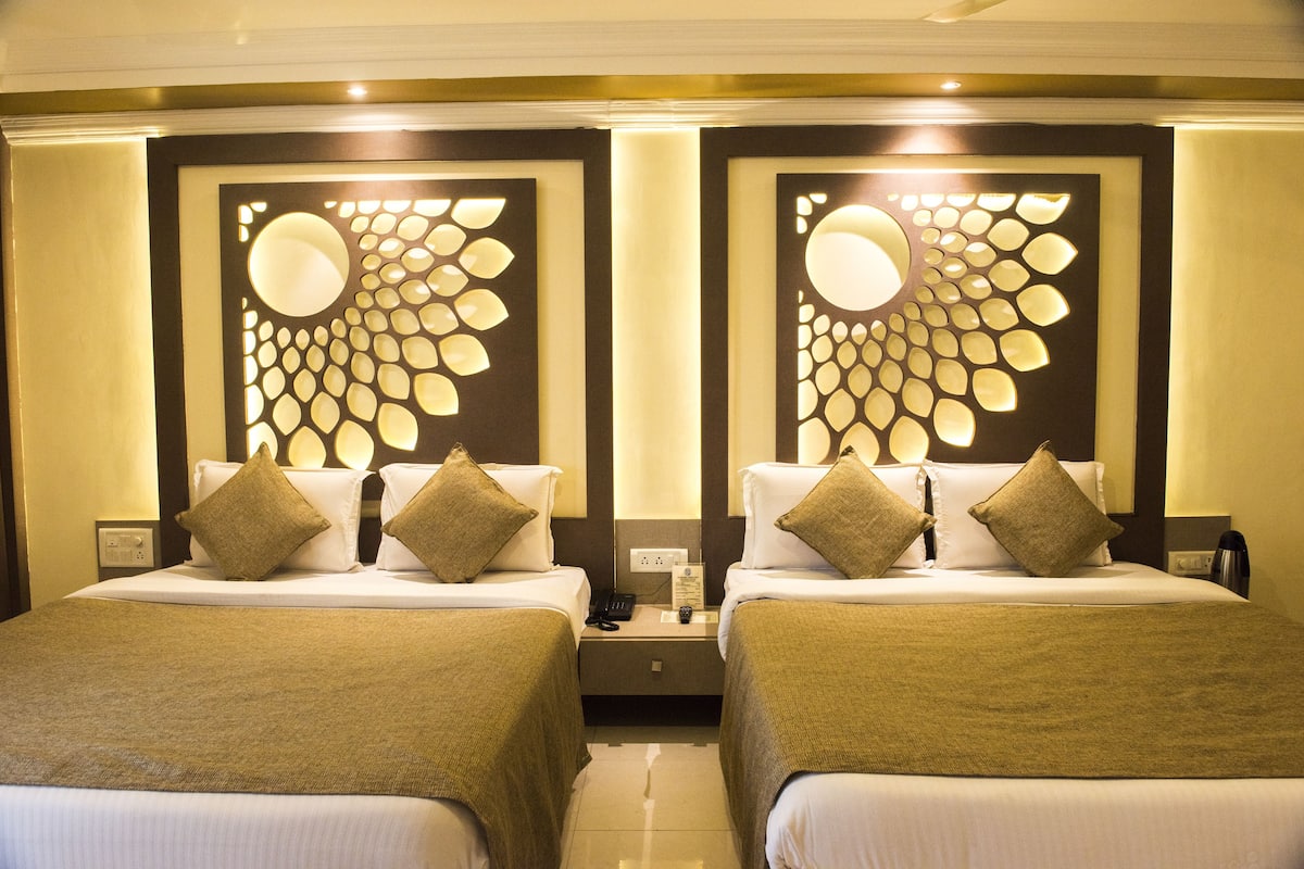 A hotel room with two single beds, each with a headboard, bedside tables, and a lamp.