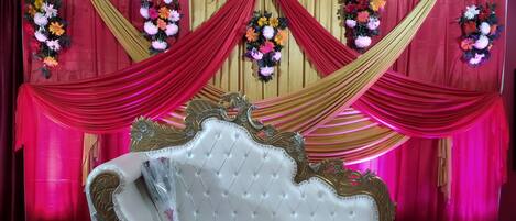 Un escenario con un sofá blanco, cortinas rojas y doradas, y arreglos florales.