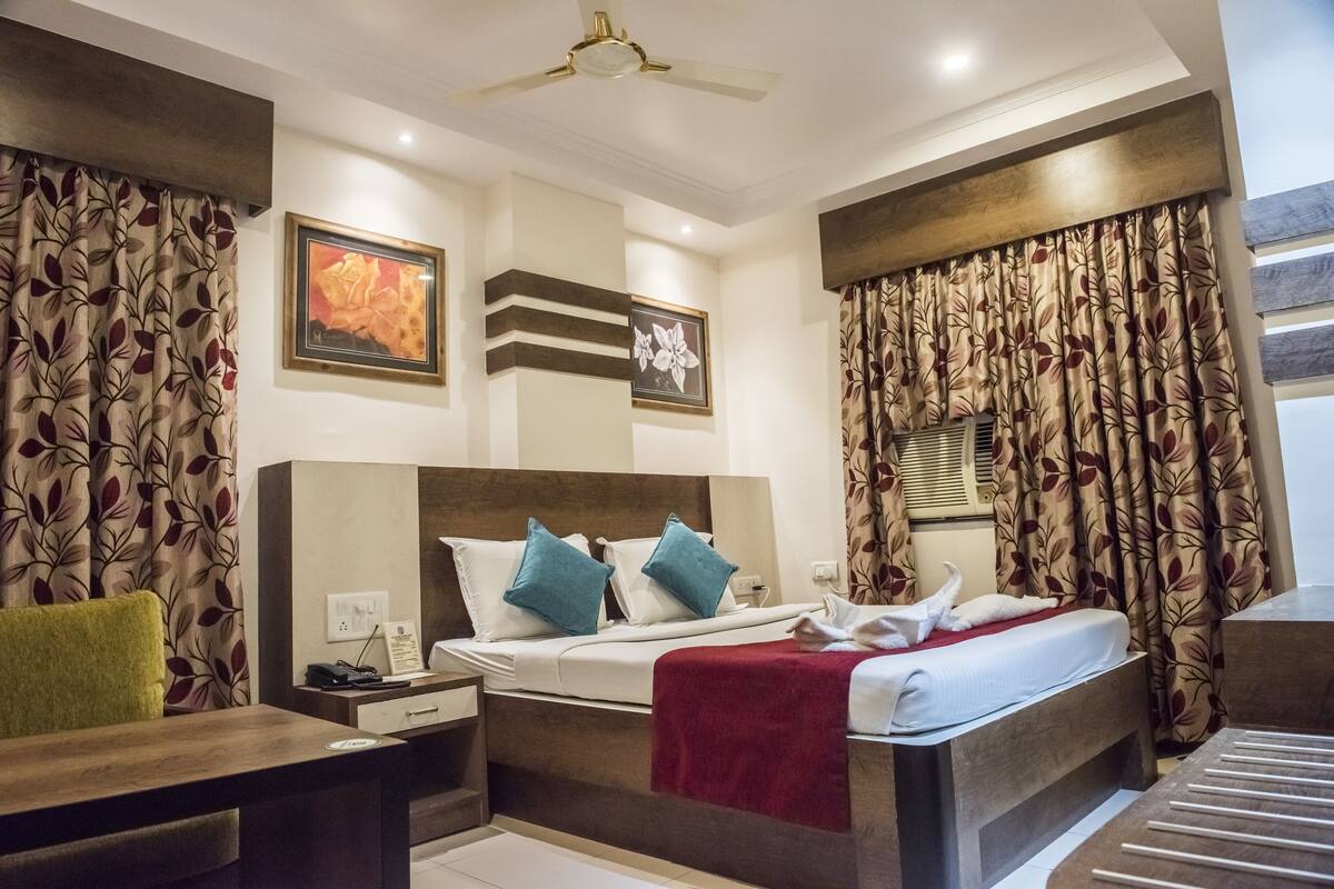 A hotel room with a bed, a desk, a chair, a ceiling fan, and curtains.