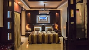 A modern bedroom with a large bed, two bedside tables, a ceiling fan, and a mounted TV. - Hotel Pushpak (Bhubaneshwar)