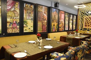 Un restaurant où les tables sont dressées pour le service, et dont les murs sont ornés d’œuvres d’art traditionnelles.