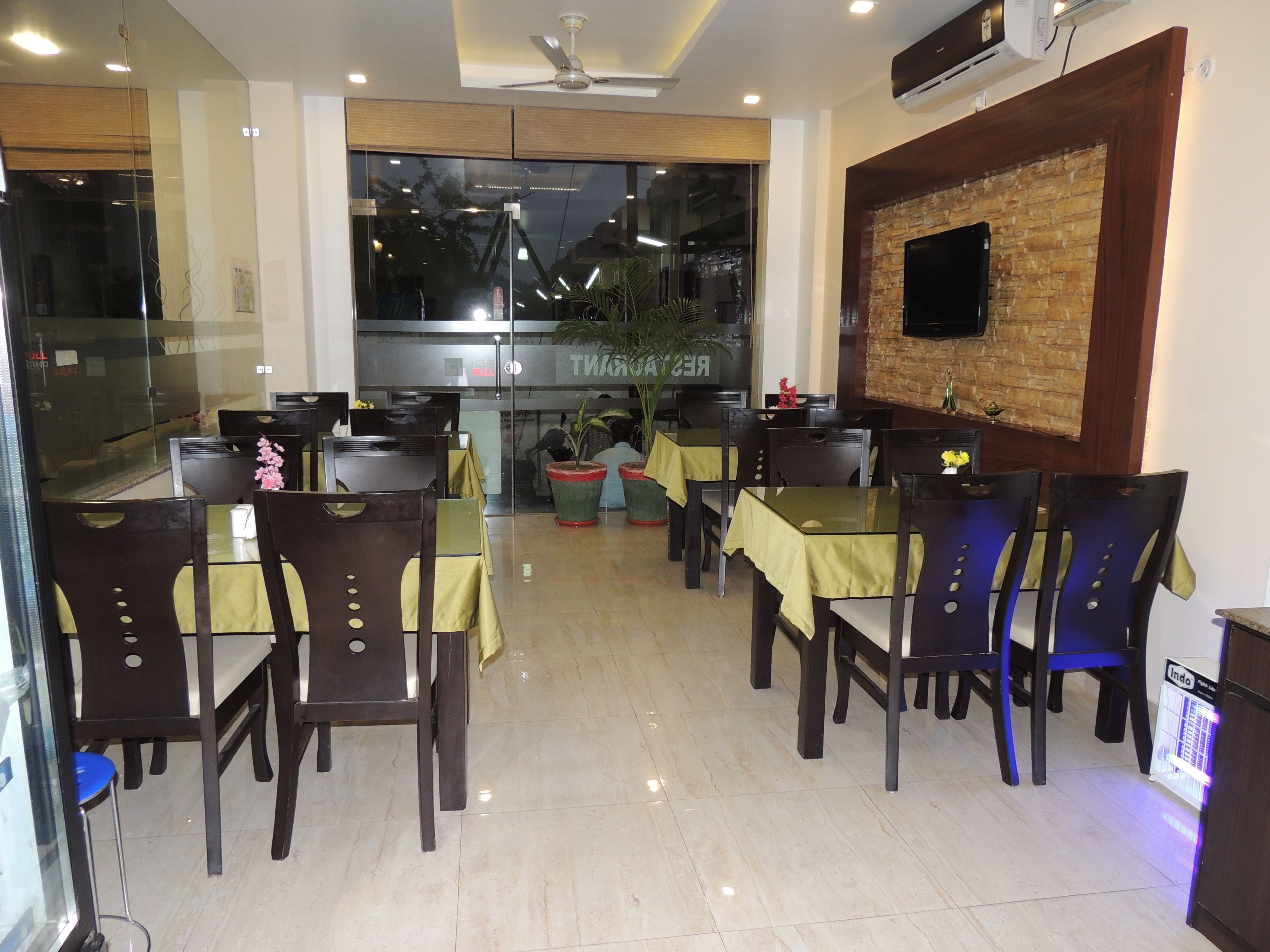 A restaurant with tables and chairs, a brick wall, and a television mounted on the wall.