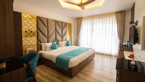 A modern bedroom with a large bed, a ceiling fan, a wooden floor, and a decorative wall panel. - Hotel Yog Vashishth (Yamkeshwar)