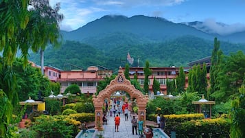A garden pathway leading to a building with a traditional archway, surrounded by lush greenery and a mountain backdrop.