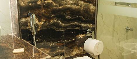 Een badkamer met een marmeren wand, toilet, douche en wastafel.
