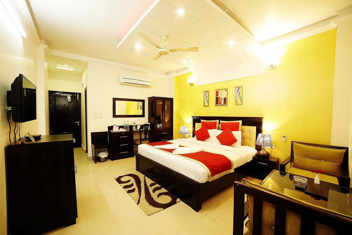 A hotel room with a bed, bedside tables, a desk, a TV, a wardrobe, and a ceiling fan.