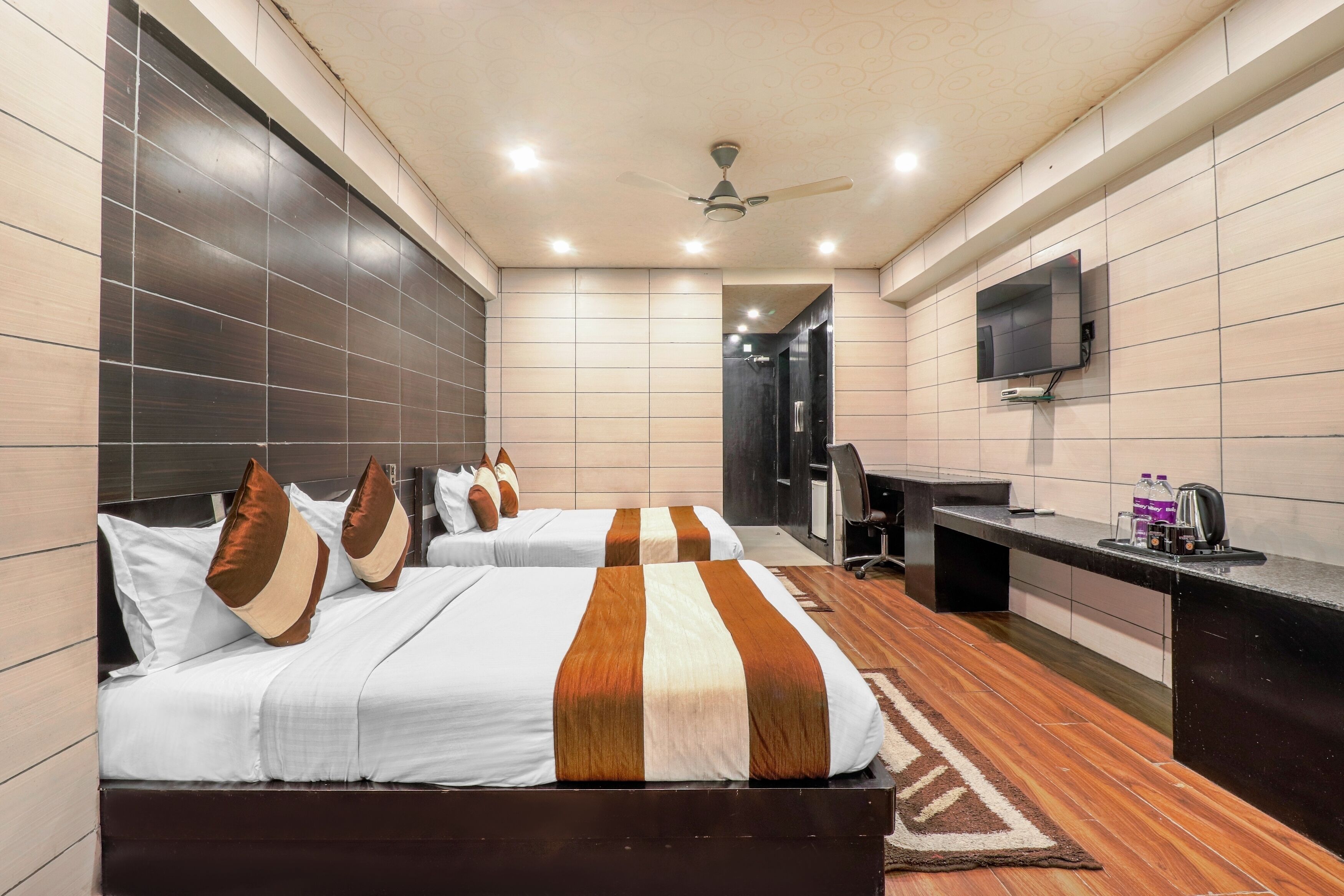 A hotel room with two beds, a desk, a TV, and a ceiling fan.