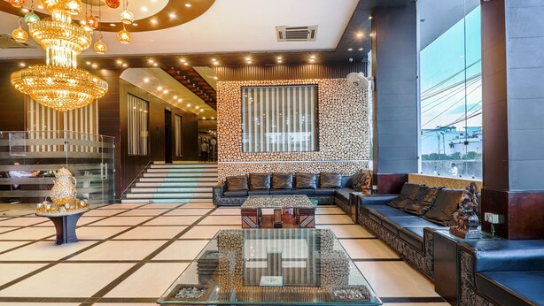 A modern lobby with a glass coffee table, a seating area with sofas, a staircase, and a decorative chandelier. - Hotel Grand Shiva (Haridwar)
