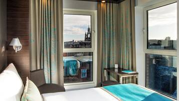 A hotel room with a bed, a desk, a chair, and a window with a city view.
