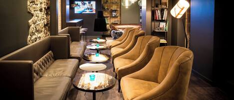 A modern lounge area with leather sofas and armchairs, a coffee table, and a bookshelf.