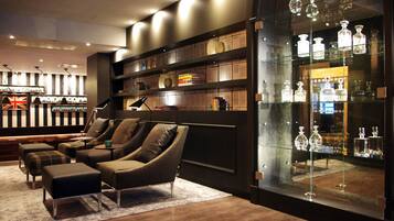 A modern lounge area with leather sofas, a glass display case of bottles, and a bookshelf.