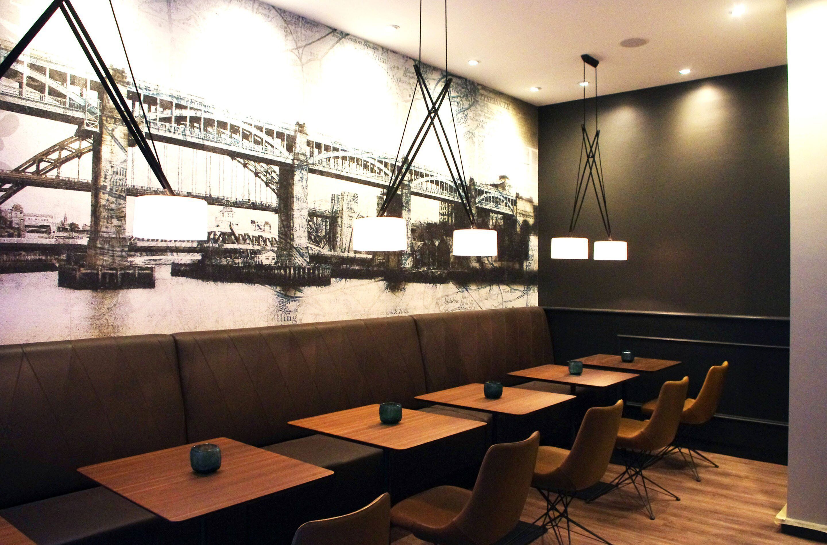 Un restaurant décoré d’une fresque représentant un pont, avec des banquettes, des tables et des luminaires suspendus.