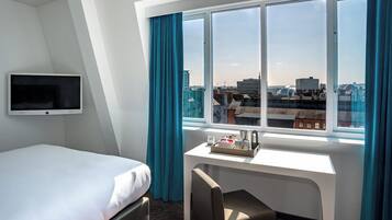Ein Hotelzimmer mit Bett, Schreibtisch mit Stuhl, Fernseher und einem Fenster mit Vorhängen.