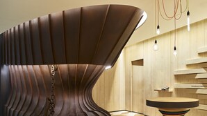 A modern interior with a unique curved metallic structure, a round wooden table, and a geometric patterned floor. - Hotel Indigo Kaohsiung Central Park by IHG (Kaohsiung)