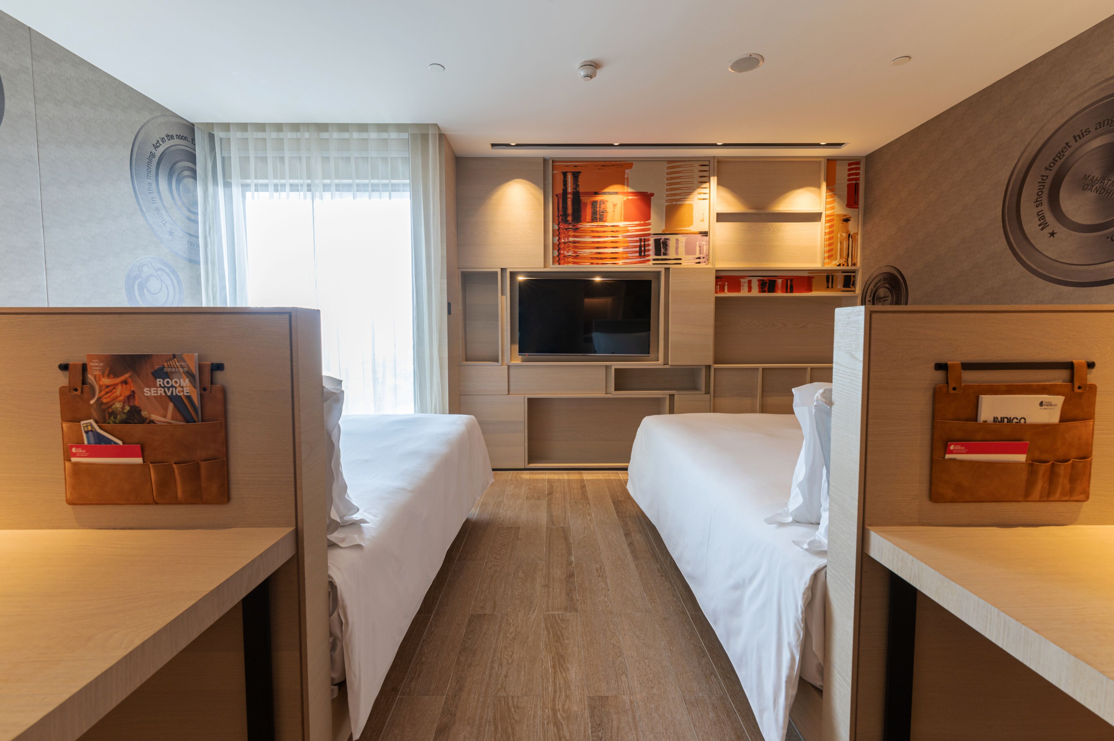 A hotel room with two single beds, a TV, a minibar, and a small desk area.