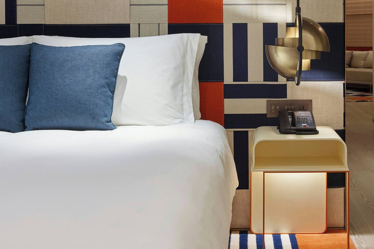 Une chambre d’hôtel avec un lit, une table de chevet avec un téléphone et un mur orné d’un motif géométrique.