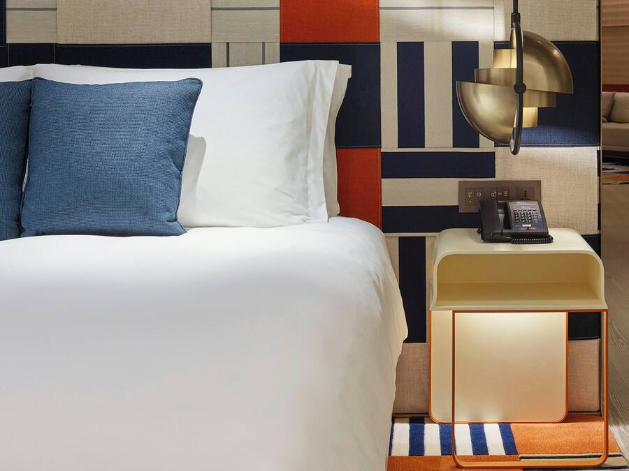 Ein Hotelzimmer mit einem Bett, einem Nachttisch mit Telefon und einer Wand mit geometrischem Muster.