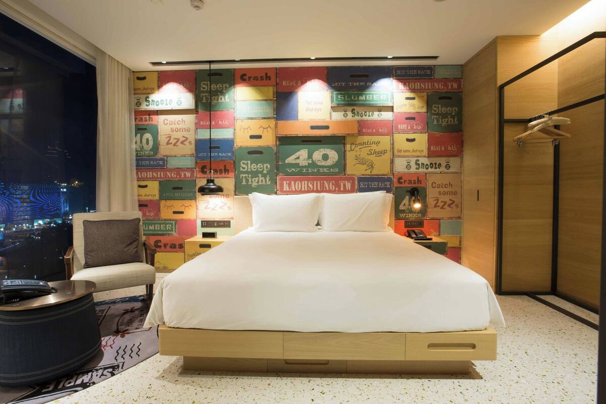 Une chambre d’hôtel avec un lit, une chaise, une petite table et une vue sur la ville la nuit.