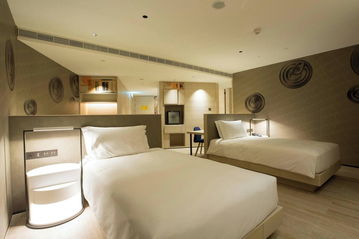 Une chambre d’hôtel avec deux lits, un bureau, une chaise et une petite kitchenette.
