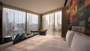A hotel room with a large bed, a desk, and a view of the city through sheer curtains. - Hotel Indigo Kaohsiung Central Park by IHG (Kaohsiung)