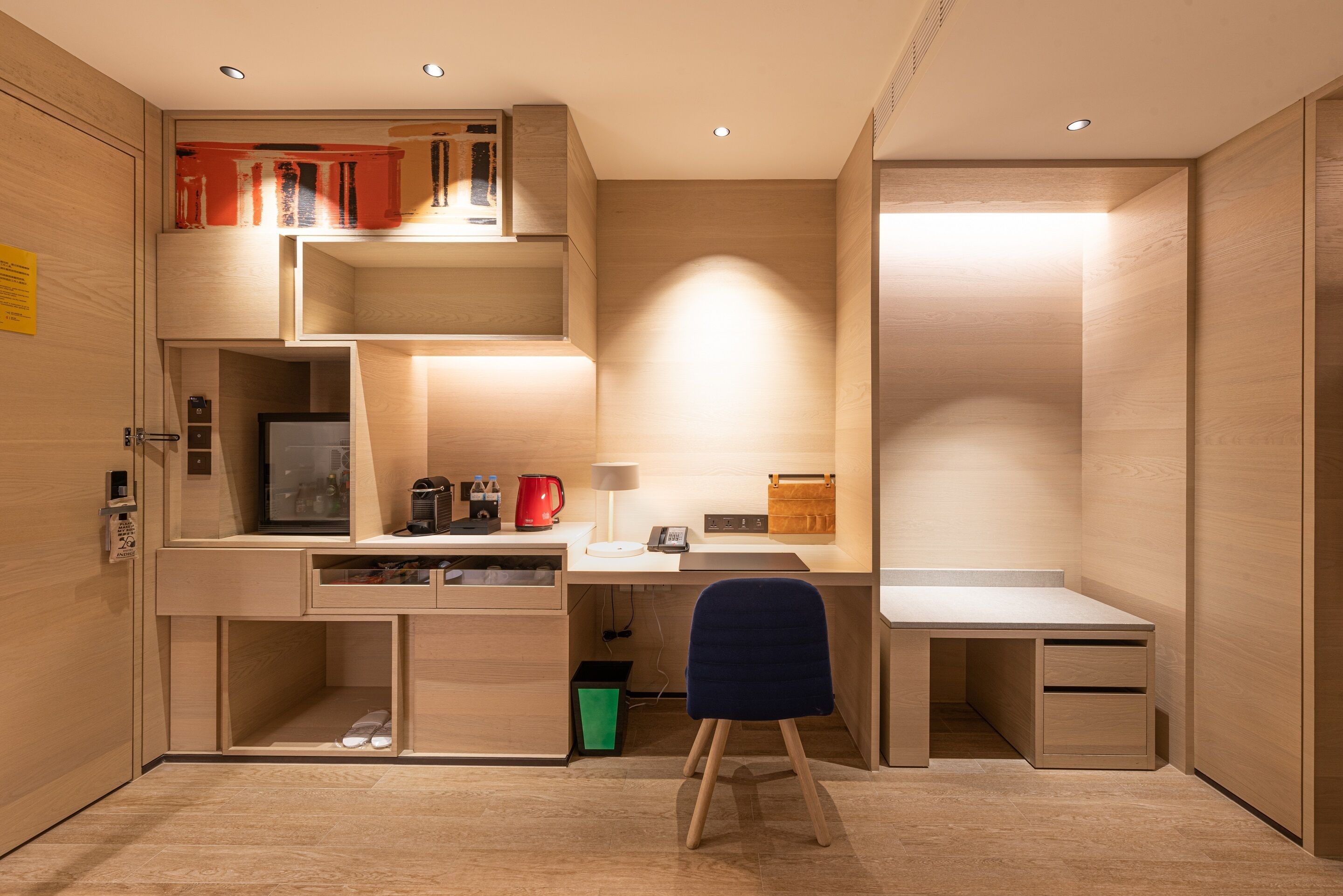 A compact, modern room with a built-in desk, a chair, and a small seating area.