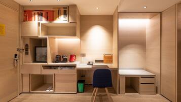 A compact, modern room with a built-in desk, a chair, and a small seating area.