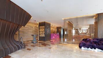 A modern lobby with a reception desk, a seating area, and a bar.
