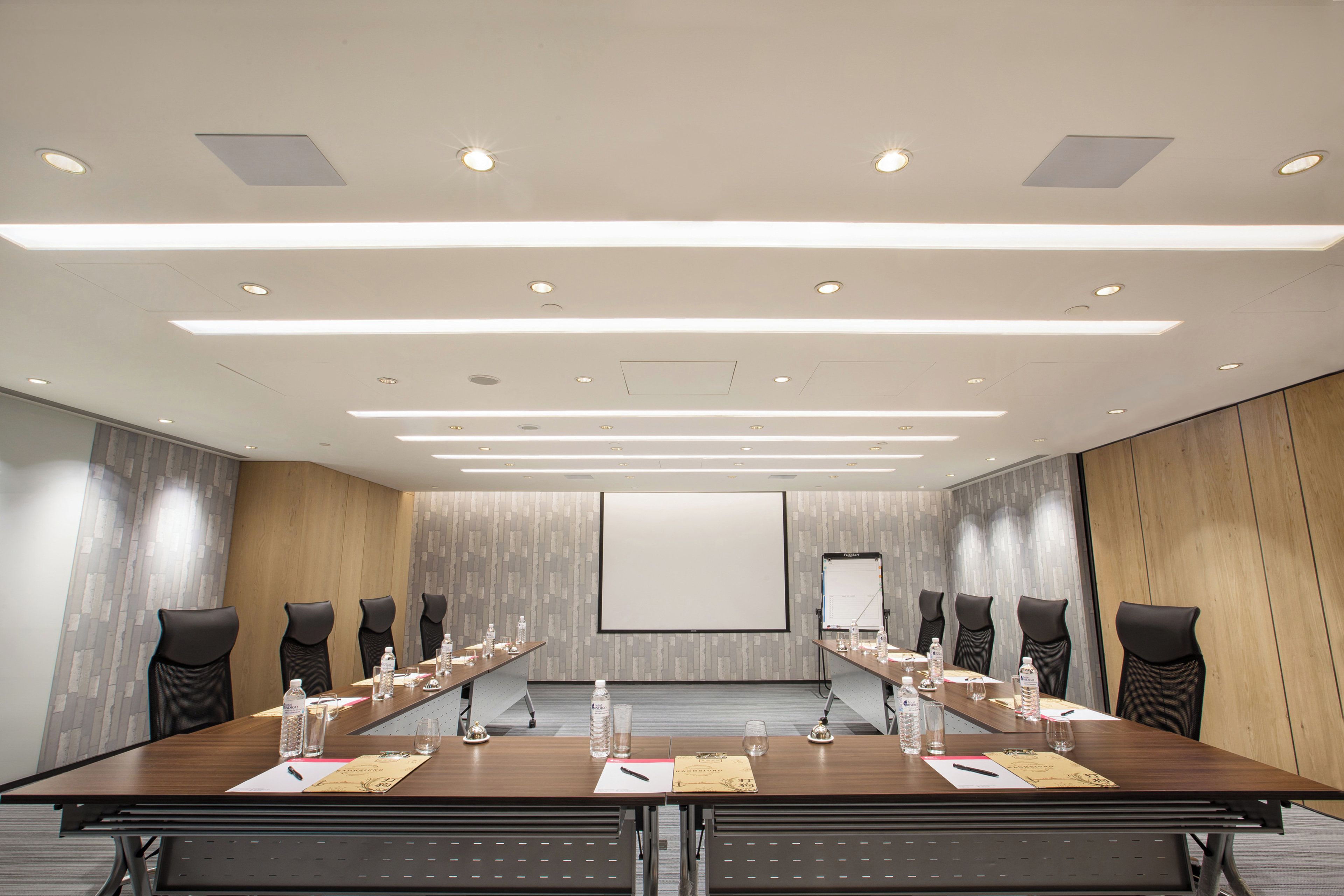 A conference room with a long table, chairs, a projector screen, and a whiteboard.