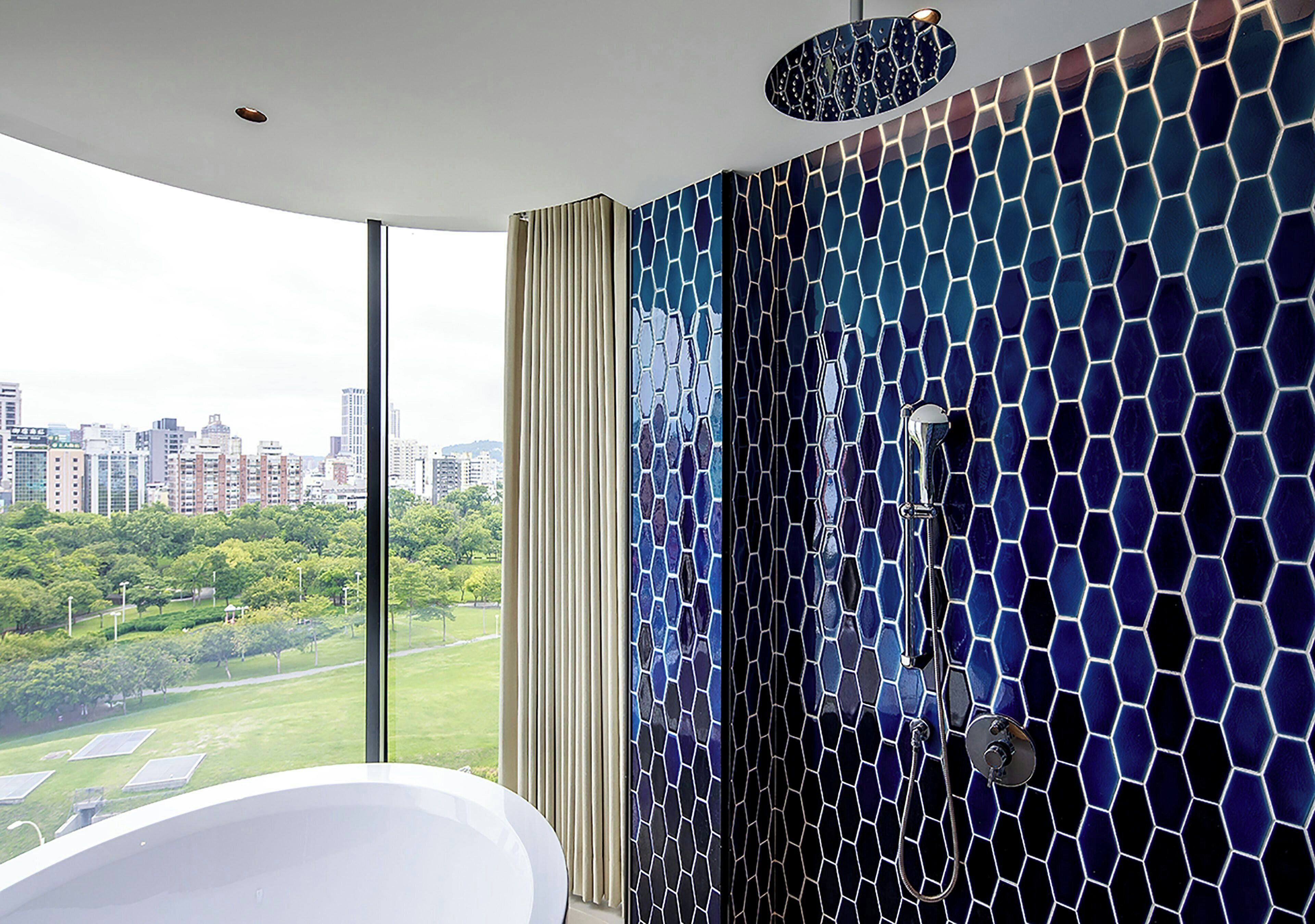 A modern bathroom with a large window, a white bathtub, and a shower with a mosaic tile wall.