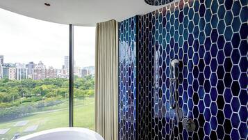 A modern bathroom with a large window, a white bathtub, and a shower with a mosaic tile wall.