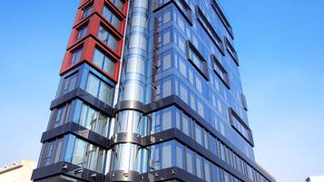 Un edificio moderno de varios pisos con fachada de vidrio, un marcado acento rojo en el lado izquierdo y un elemento de diseño curvo.