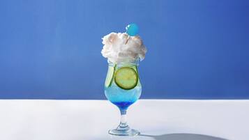 A cocktail glass with a blue liquid, a lime slice, and a blue spherical garnish on a white surface against a blue background.