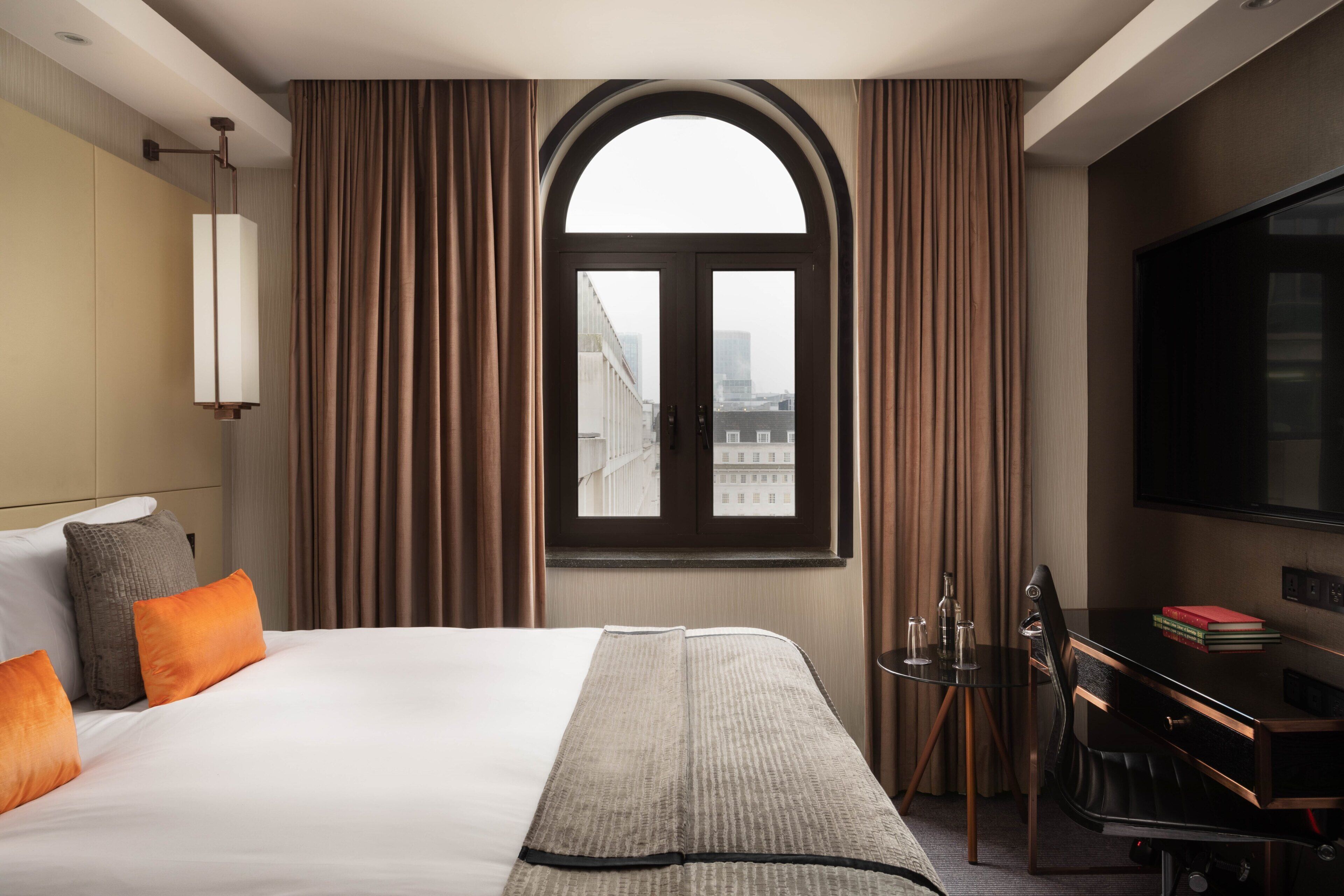 Ein Hotelzimmer mit einem großen Bett, einem Schreibtisch mit Stuhl, einem Flachbildfernseher und einem Fenster mit Vorhängen.