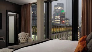 A modern hotel room with a large bed, a chair, and a view of a cityscape through large windows. - Montcalm Royal London House, Autograph Collection (London)