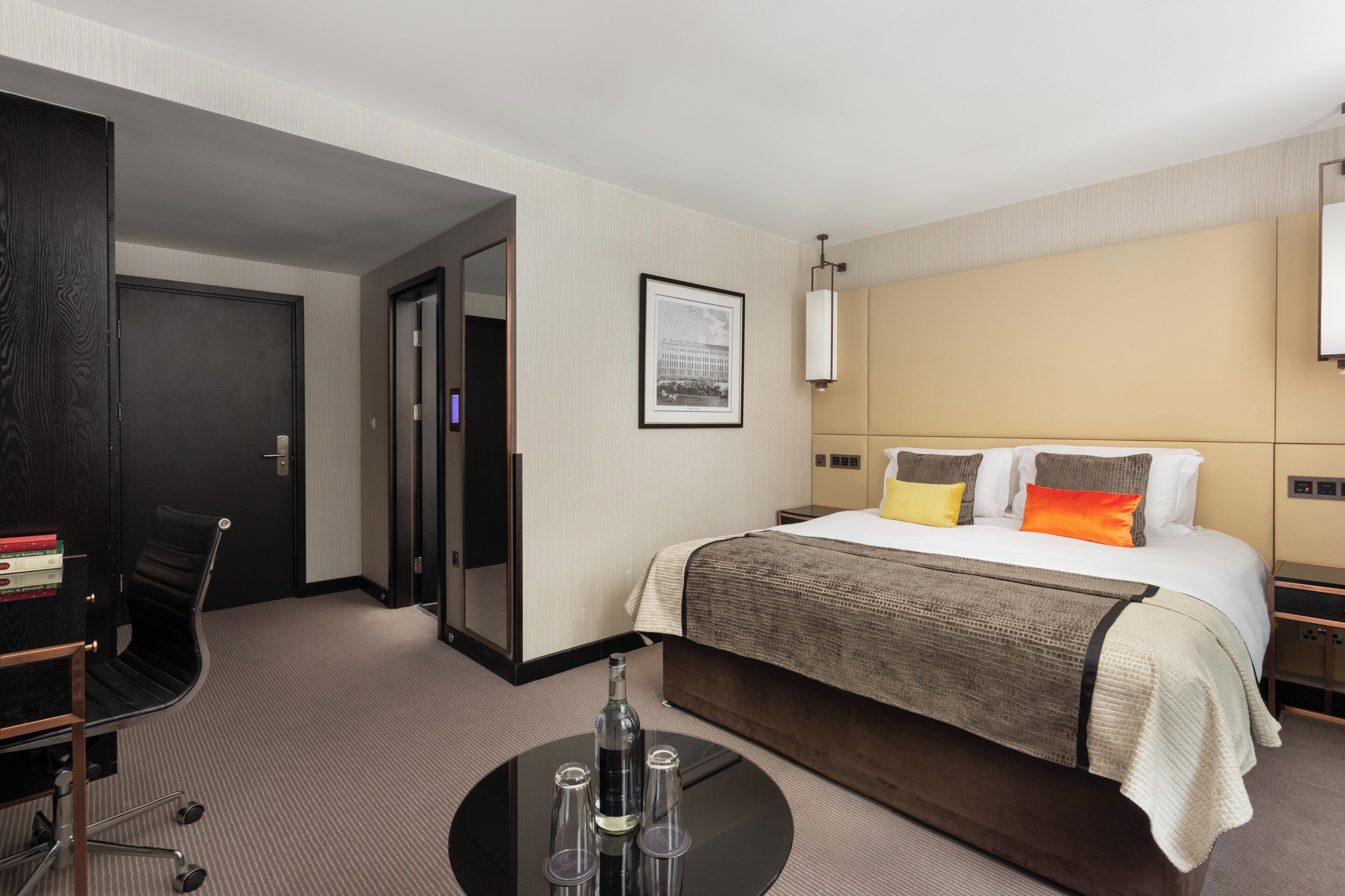 Habitación de hotel con cama, escritorio, silla y mesa redonda con una botella y vasos.
