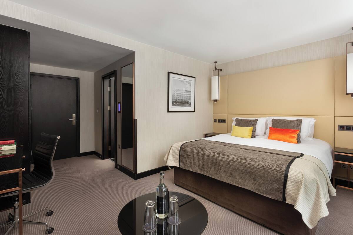 Habitación de hotel con cama, escritorio, silla y mesa redonda con una botella y vasos.