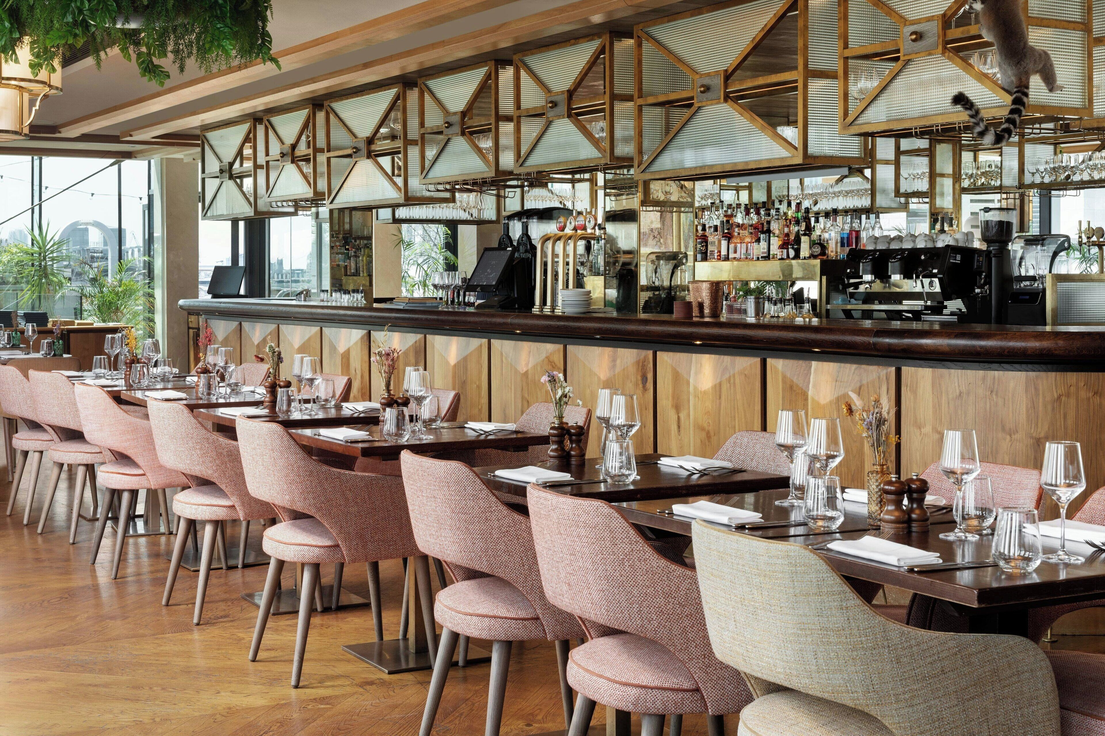 A restaurant with a long bar, multiple tables, and chairs.