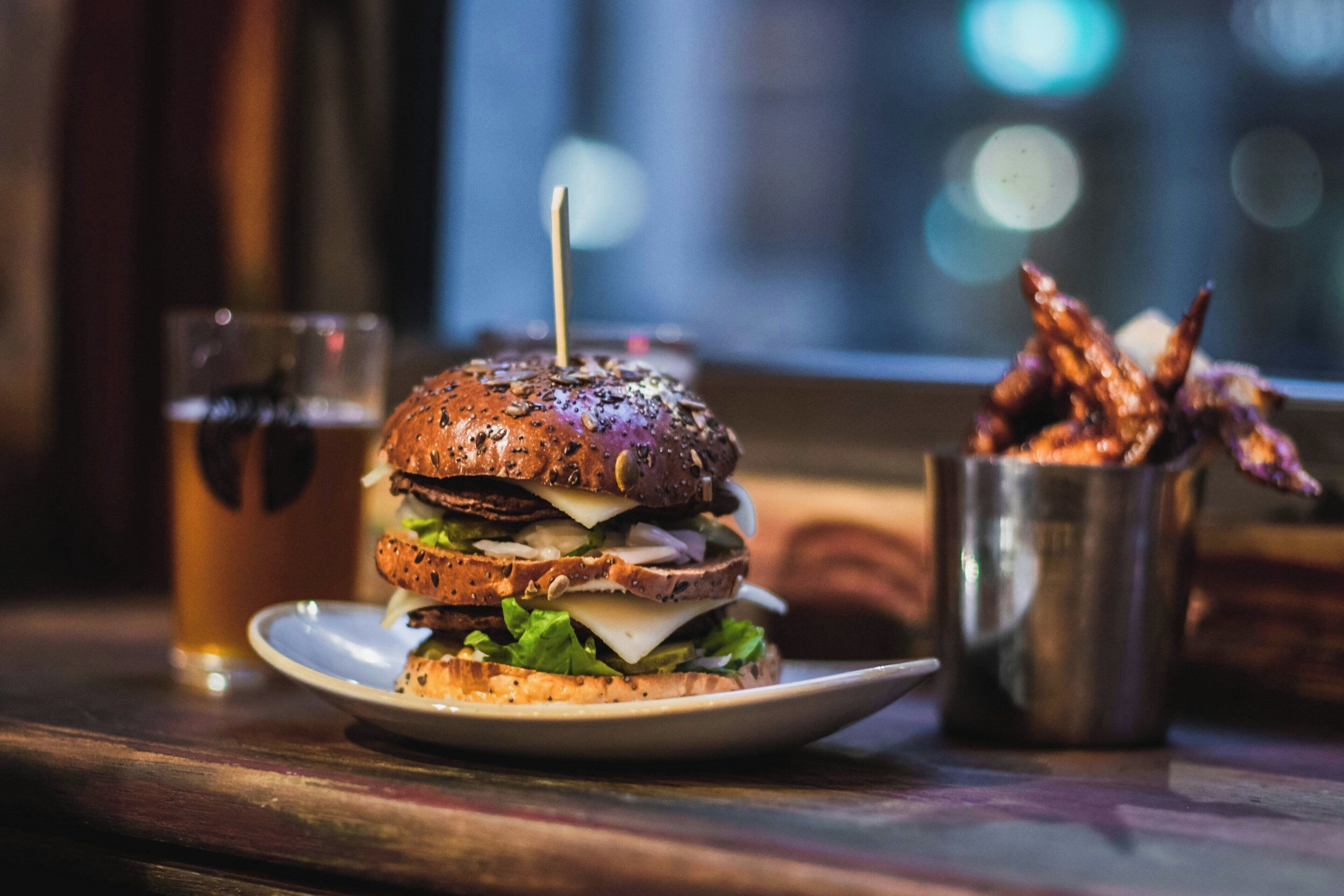 Ein Burger mit Sesambrötchen, einem Zahnstocher und Pommes Frites auf einem Teller.