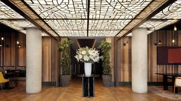 A lobby with a geometric ceiling design, wooden panel walls, and a central floral arrangement.