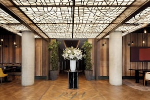 Un hall d’entrée doté d’un plafond au design géométrique, de murs recouverts de panneaux en bois et d’un arrangement floral central.