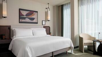 A hotel room with a large bed, a chair, a small table, and a painting on the wall.