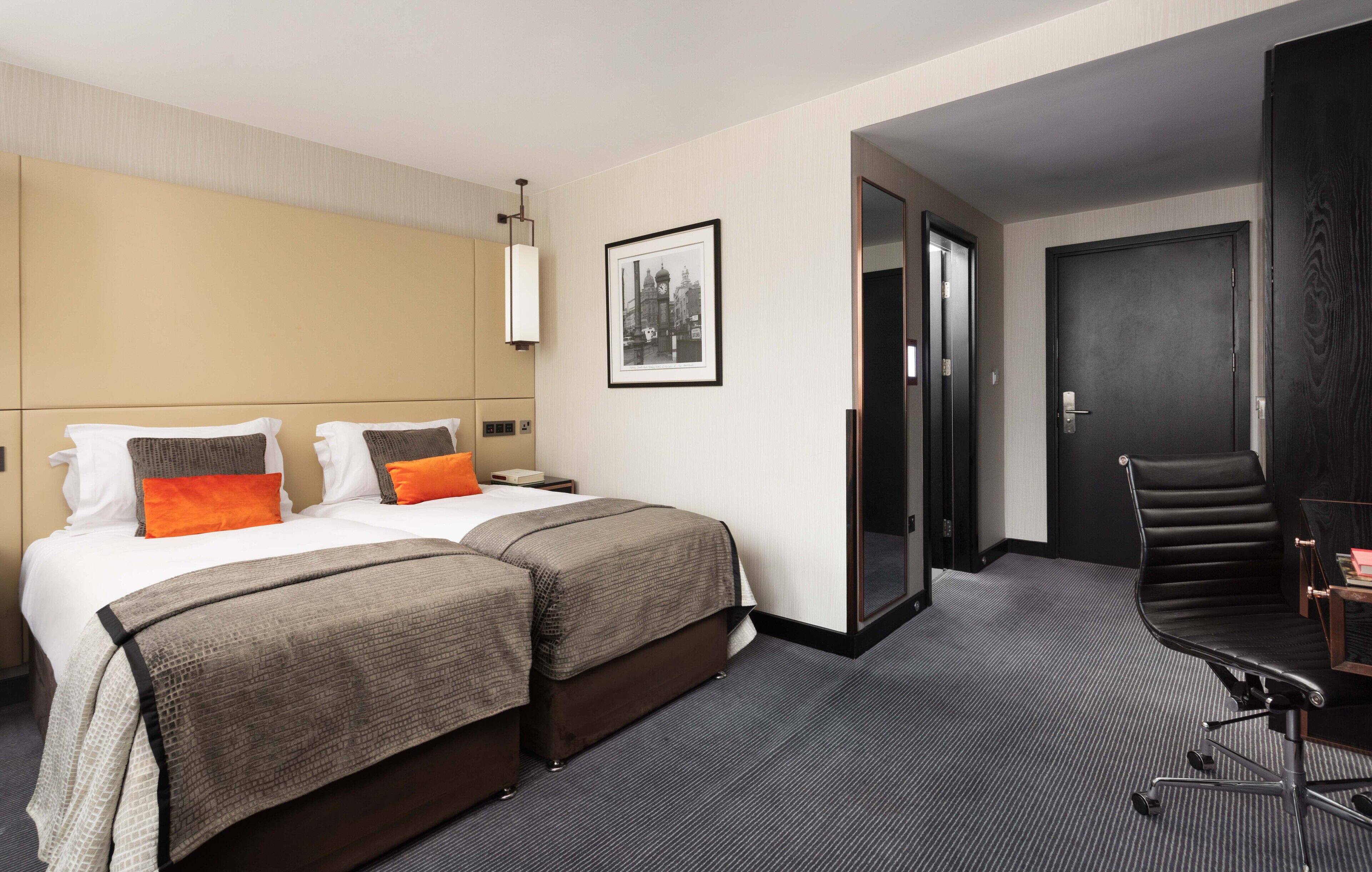 Ein Hotelzimmer mit einem großen Bett, zwei Kissen, einem Nachttisch, einem Sessel, einem Schreibtisch und einem gerahmten Bild an der Wand.