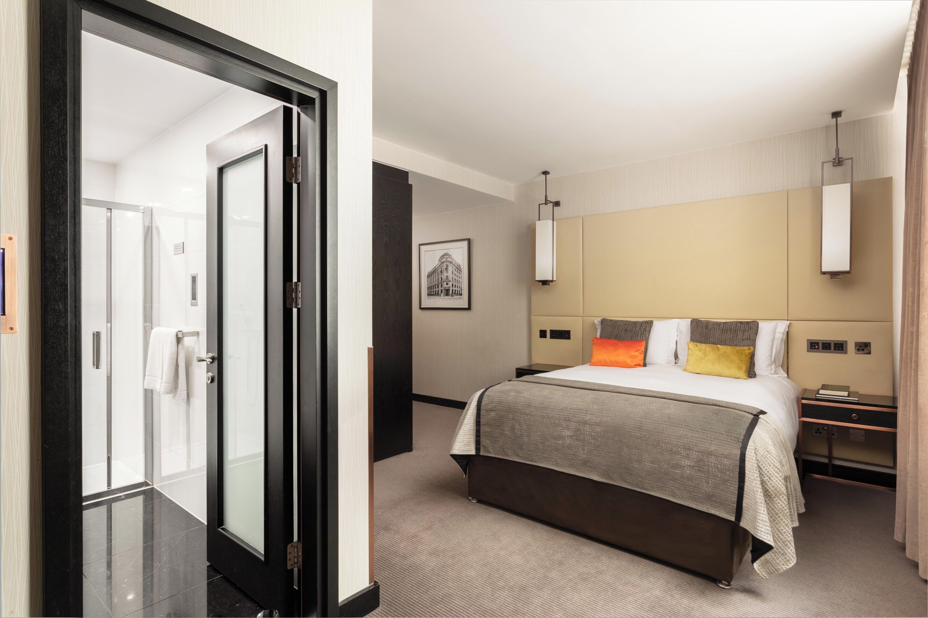 Habitación de hotel con cama, mesitas de noche, una imagen enmarcada en la pared y una puerta que da al baño.