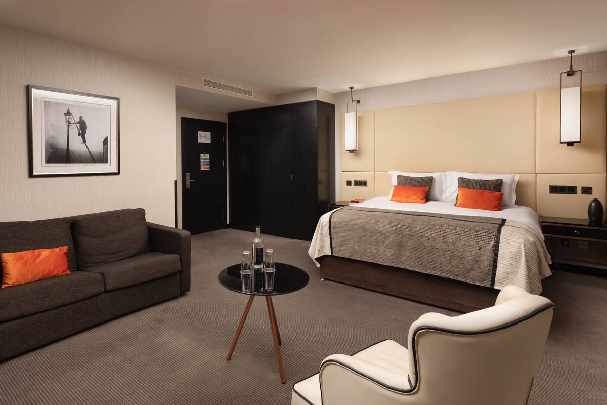 Ein Hotelzimmer mit einem Bett, einem Sofa, einem kleinen Tisch mit Gläsern und einem Sessel.